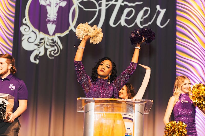 Cheerleader at a podium holding pom-poms.