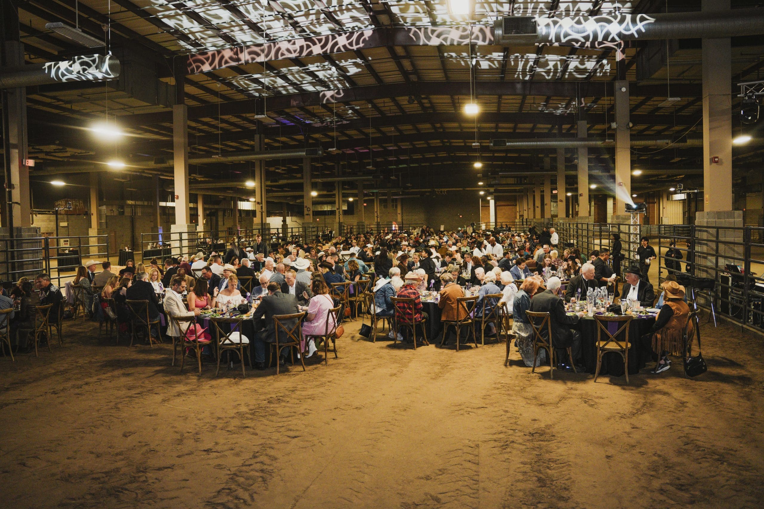 Guests seated at round tables in a large barn venue during the Avila University Steer Dinner