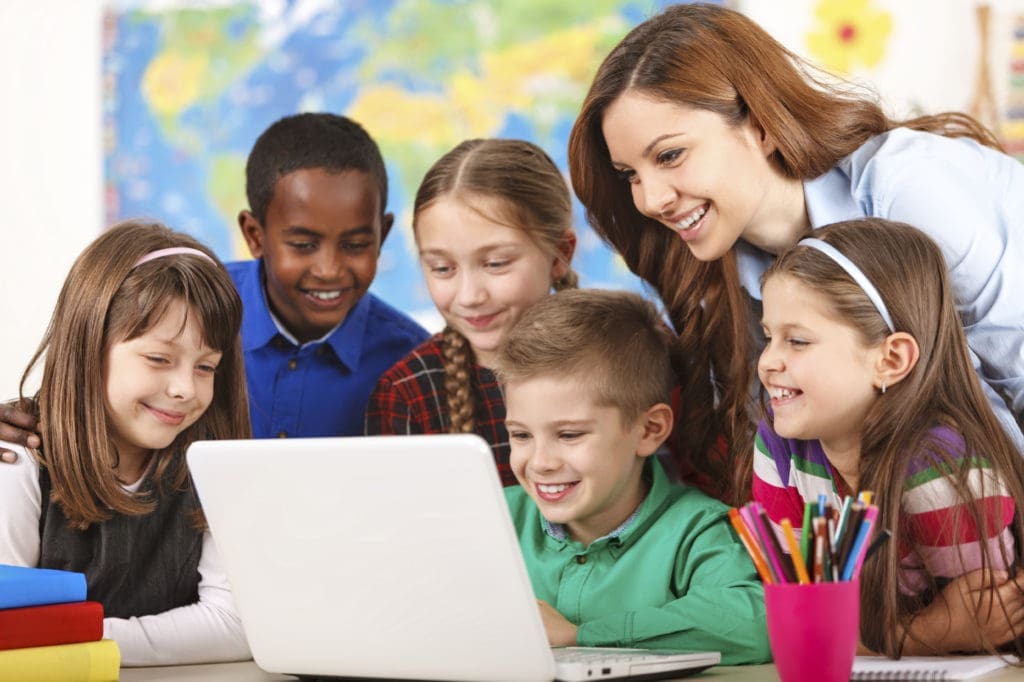 School children using laptop with teacher in the classroom